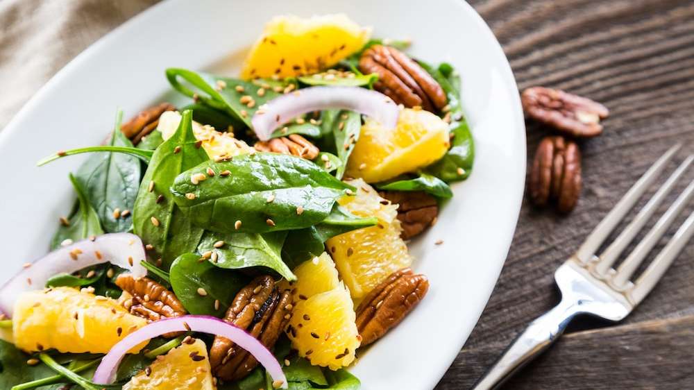 Une salade d'hiver d'épinards, d'orande,et de pacanes dressée dans une assiette ovale blanche