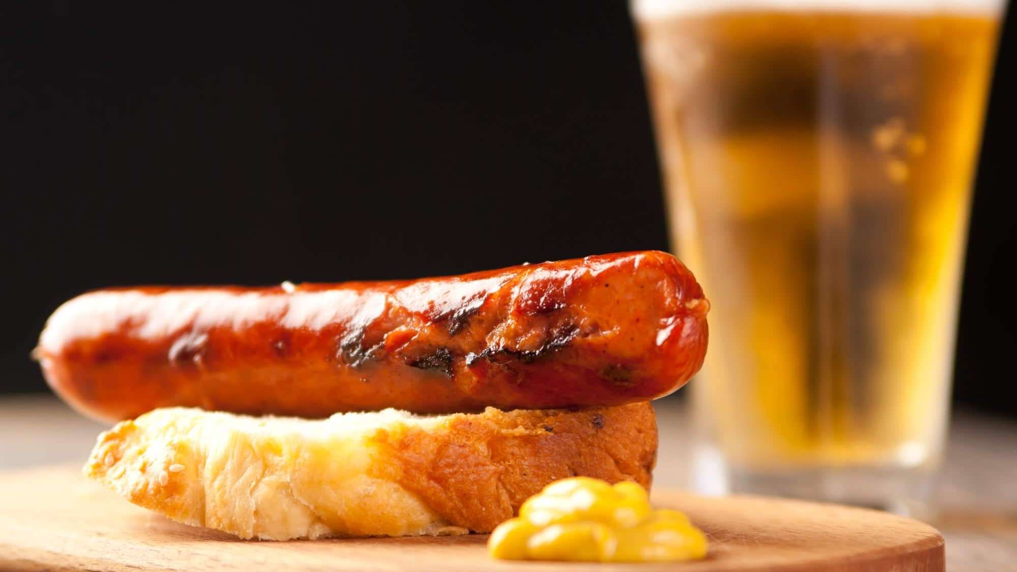 Une saucisse grillé posé sur un pain, accompagnée de moutarde jaune et d'une pinte de bière.