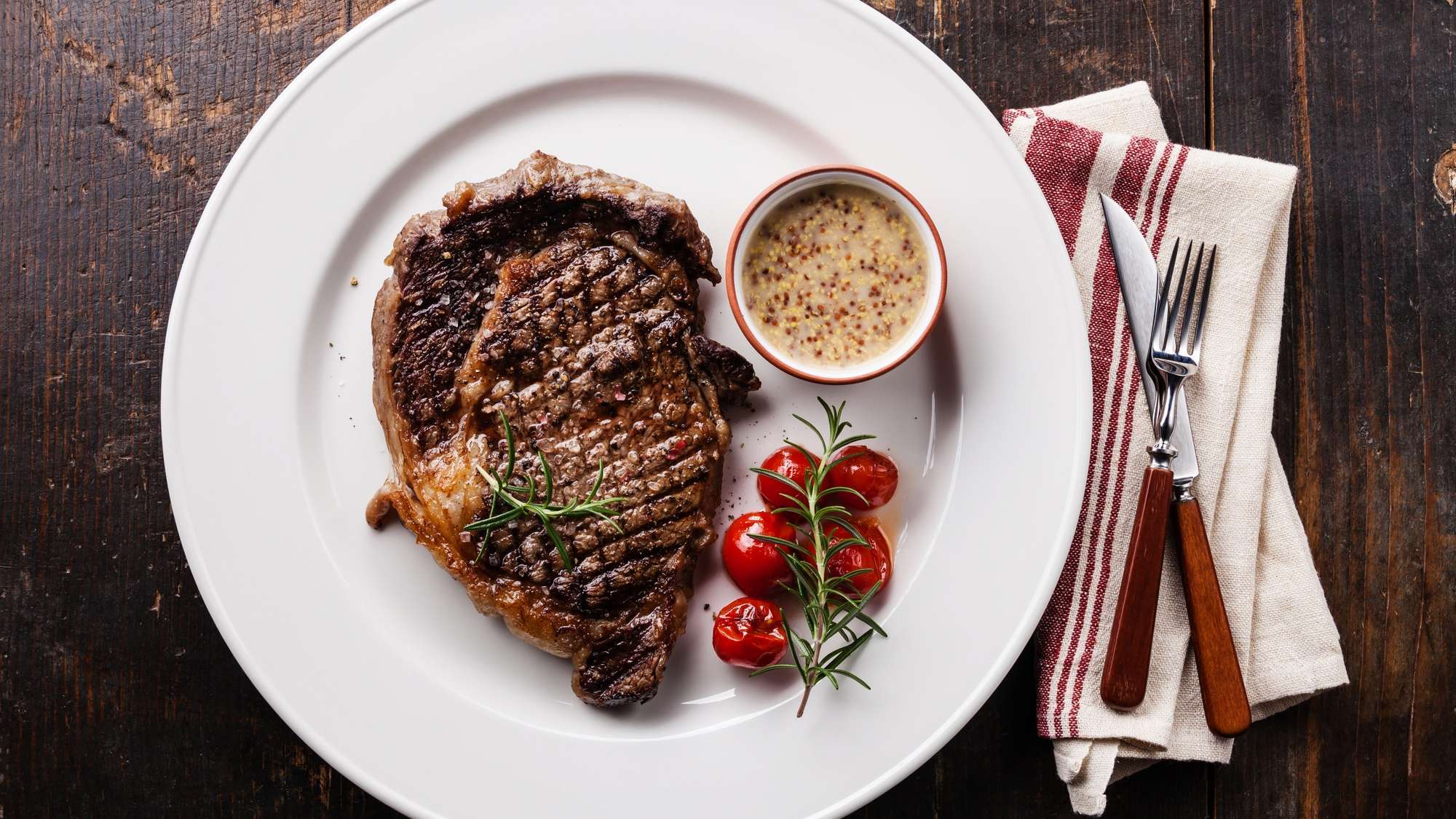 Un steak sur une assiette blanche avec un ramequin de sauce Béarnaise, posée sur une table en bois