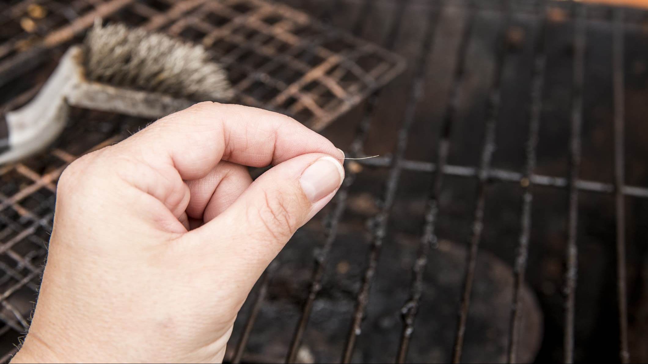 une main présente un fil de métal avec un barbecue en fond de trame