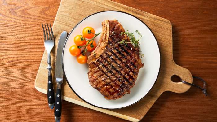 Un Rib steak préparé au BBQ repose dans une assiette blanche placée sur une planche de bois avec manche.