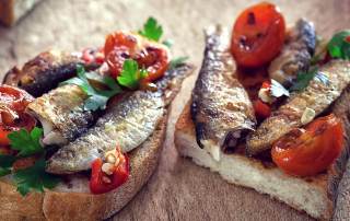 Deux tartines garnies de filets de sardine, tomates rôtie et persil