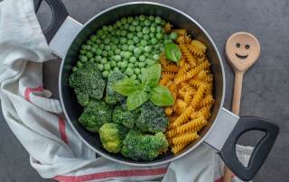 Dans une casserole, des pâtes crues avec des brocolis et petits pois congelés, garni de basilic