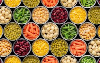 Gros plan sur des rangées de conserves ouvertes d'aliments variés: haricots verts, carottes, maïs, haricots rouges, petits pois, champignons et pois chiches