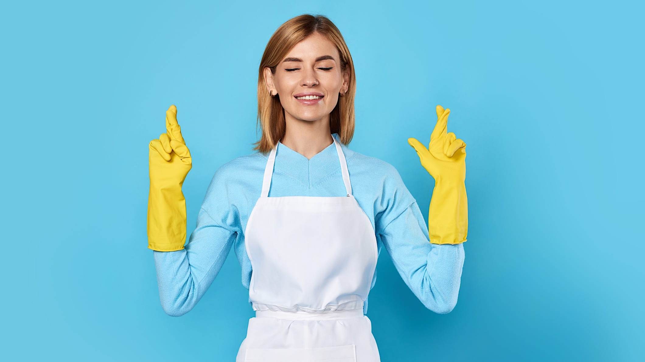Une femme avec des gants de cuisine jaunes se croisent les doigts en faisant un souhait, les yeux fermés