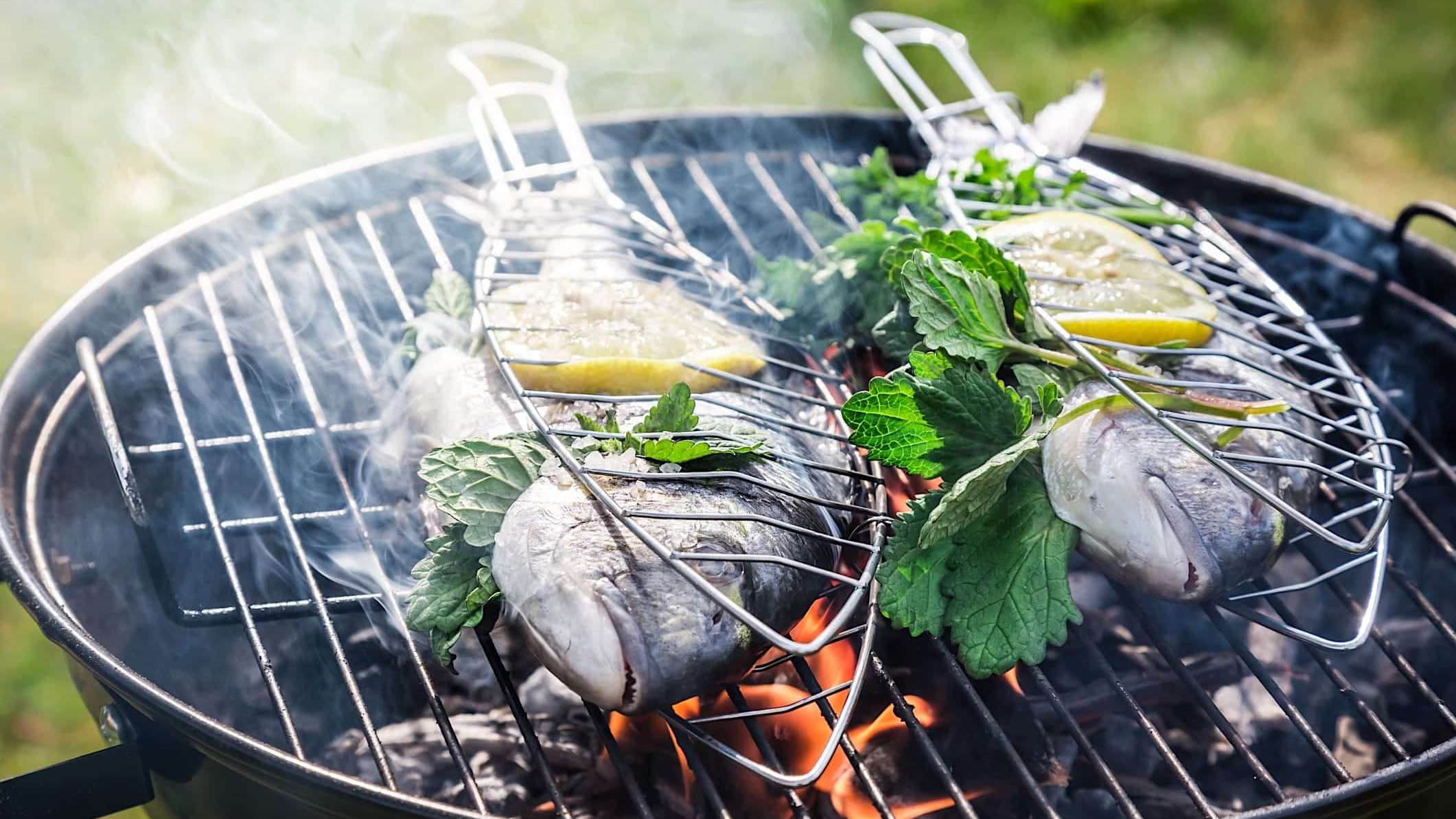 2 poissons entiers garnis d'herbes et de citron, dans des paniers à poisson, déposés sur un BBQ au charbon