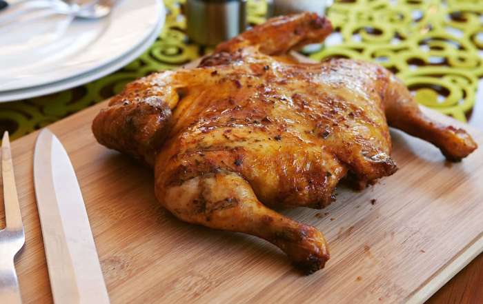 Un poulet en crapaudine grillé au BBQ, sur une planche de bois, avec un couteau de chef et une fourchette à rôti posés à côté