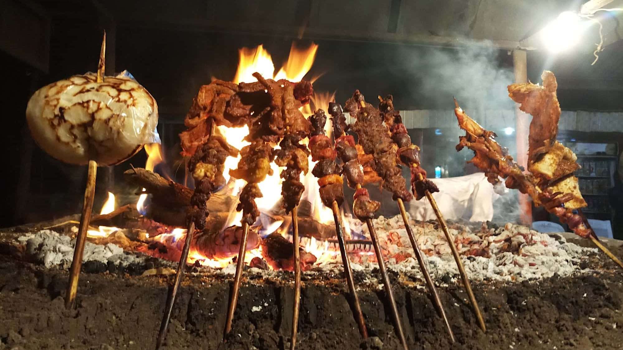 Une tête d'ail et des brochettes grillent sur un BBQ vertical africain