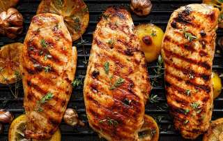 3 poitrines de poulet grillées sur le BBQ avec des tranches de citron et de l'ail grillé
