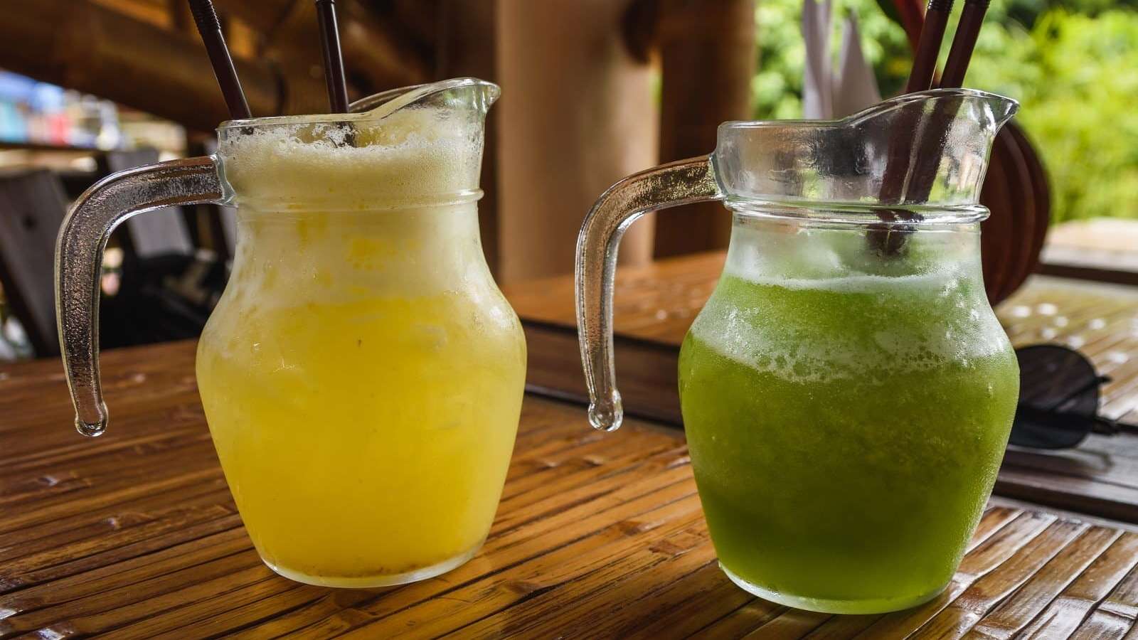 deux pichets de boissons glacées rafraîchissantes: une boisson jaune et l'autre verte. Déposés sur une table en bois à l'extérieur.
