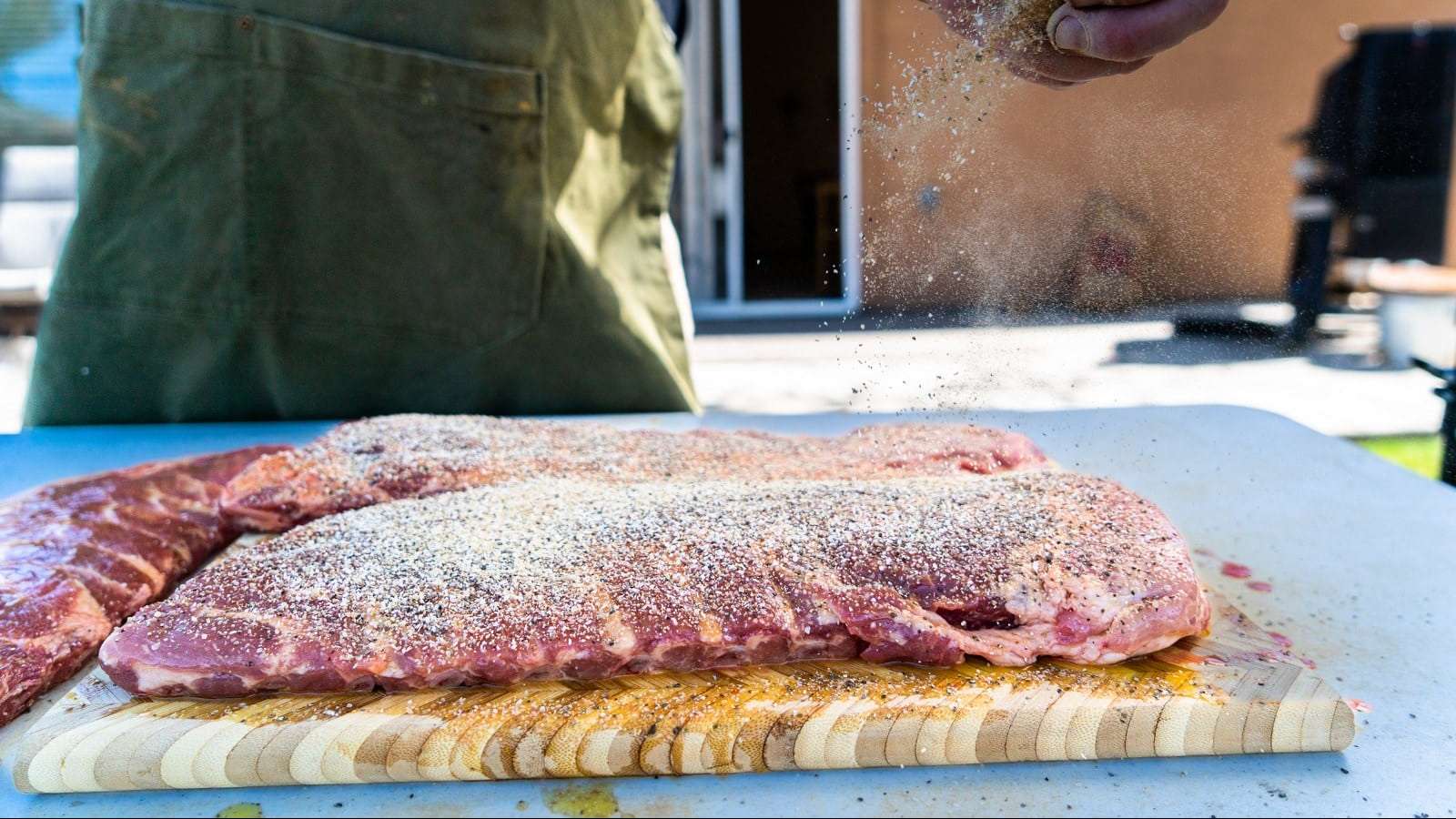 Une personne saupoudre un mélange d'épices sur des gros morceaux de côtes levées de porc cru.