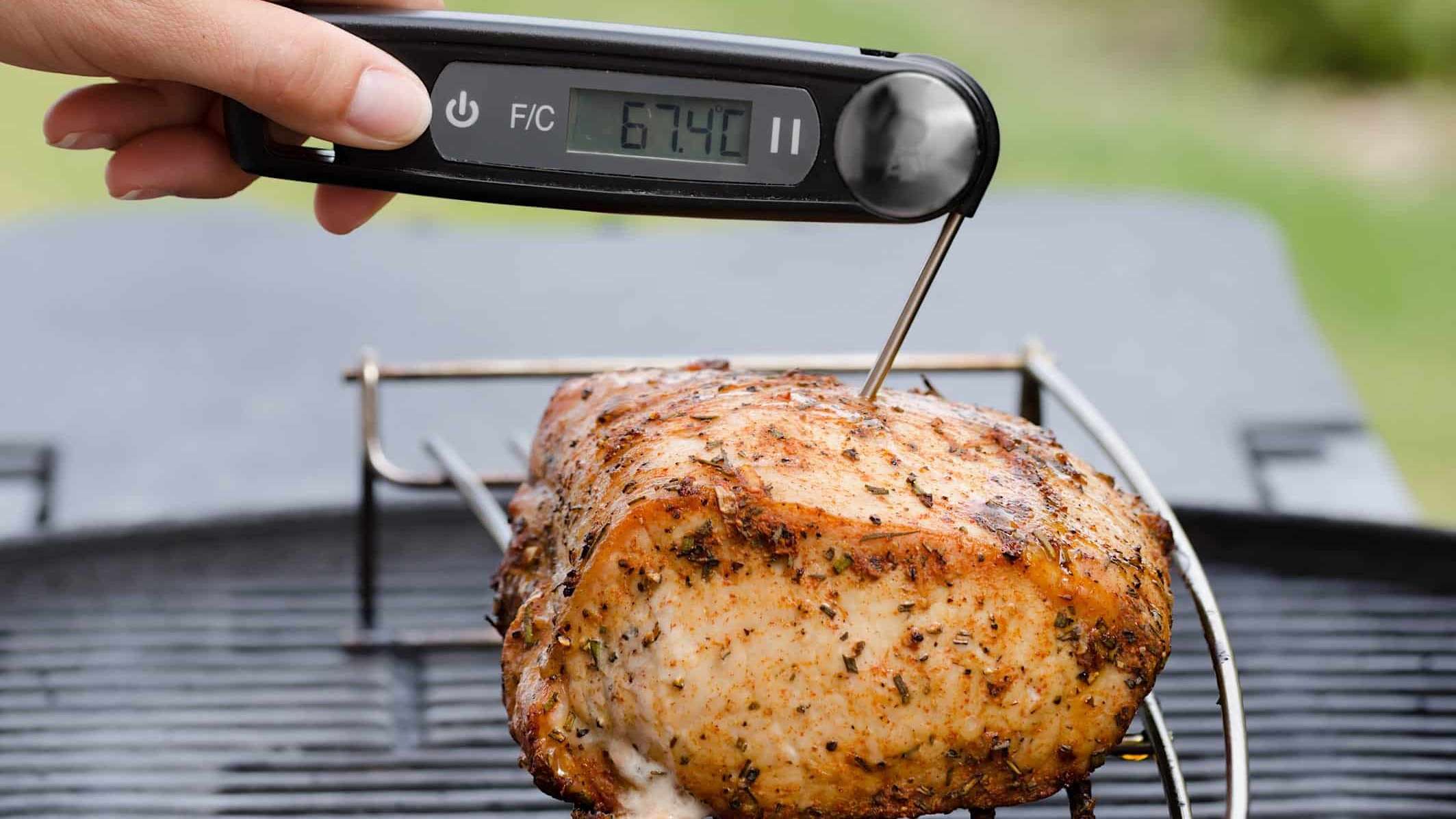 Un rôti de porc cuit est posé sur une grille et une personne prend sa température à coeur avec un thermomètre à lecture instantanée.