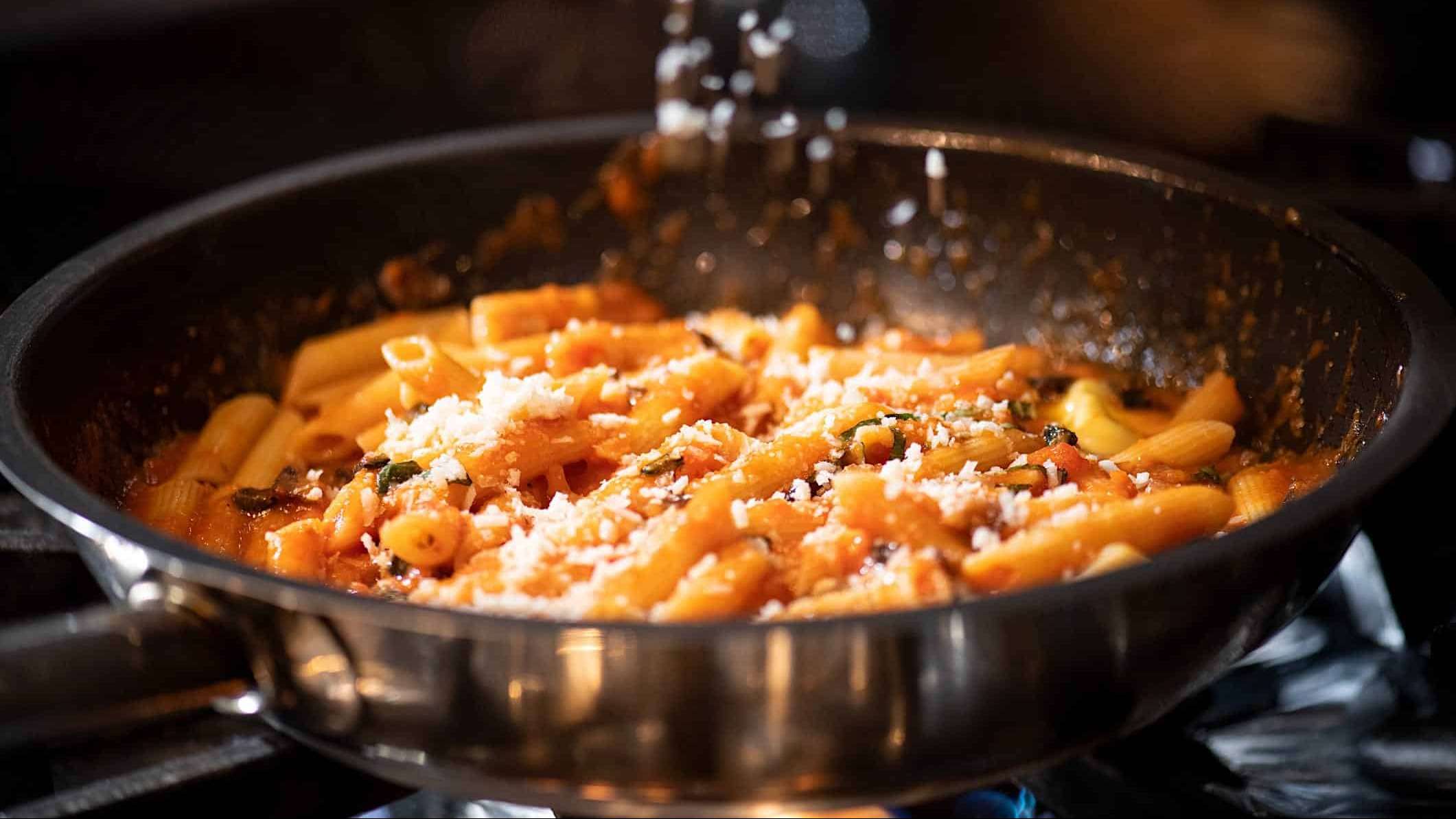 Du parmesan finement râpé est saupoudré au dessus d'un poêlon contenant des pâtes à la sauce tomate