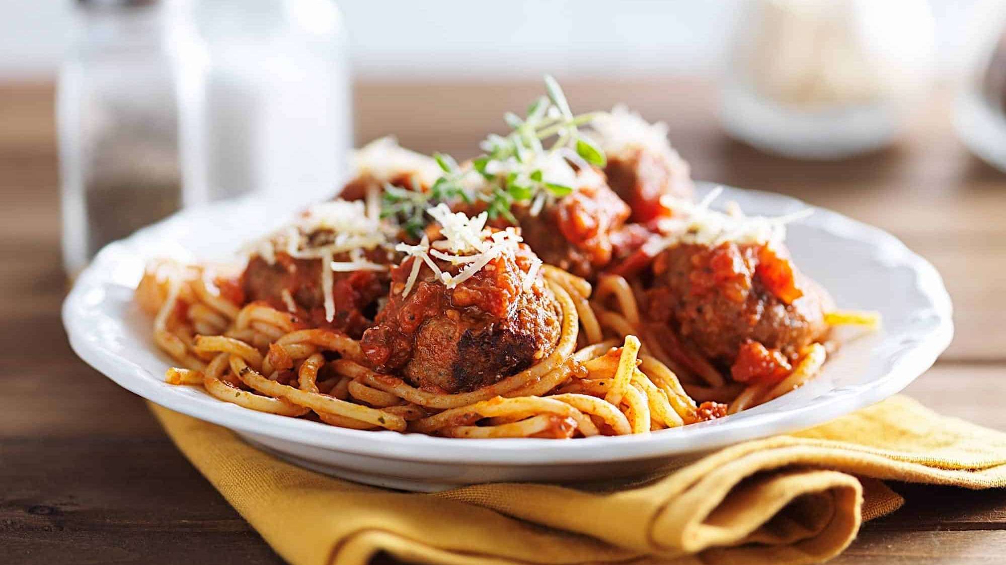 Des boulettes de viande de boeuf hachée cuites en sauce tomates sont posées sur des spaghetti, dans une assiette blanche