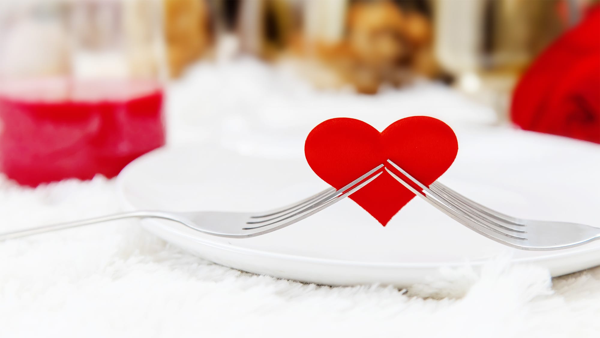 Un coeur en papier rouge est tenu par deux fourchettes pour représenter les aliments aphrodisiaques à manger à la Saint-Valentin