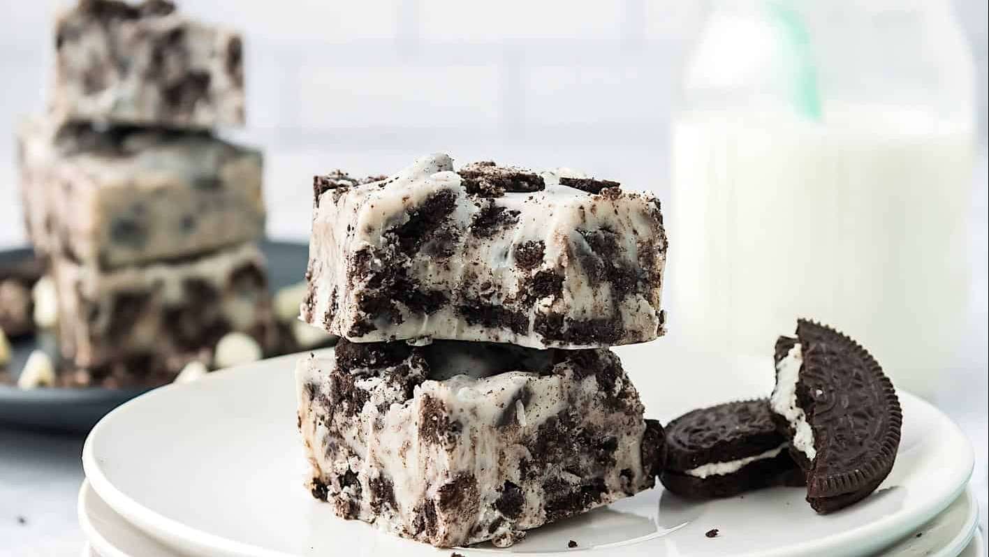Des morceaux de fudge aux biscuits au chocolat sont dressés dans une assiette, avec un verre de lait en arrière plan