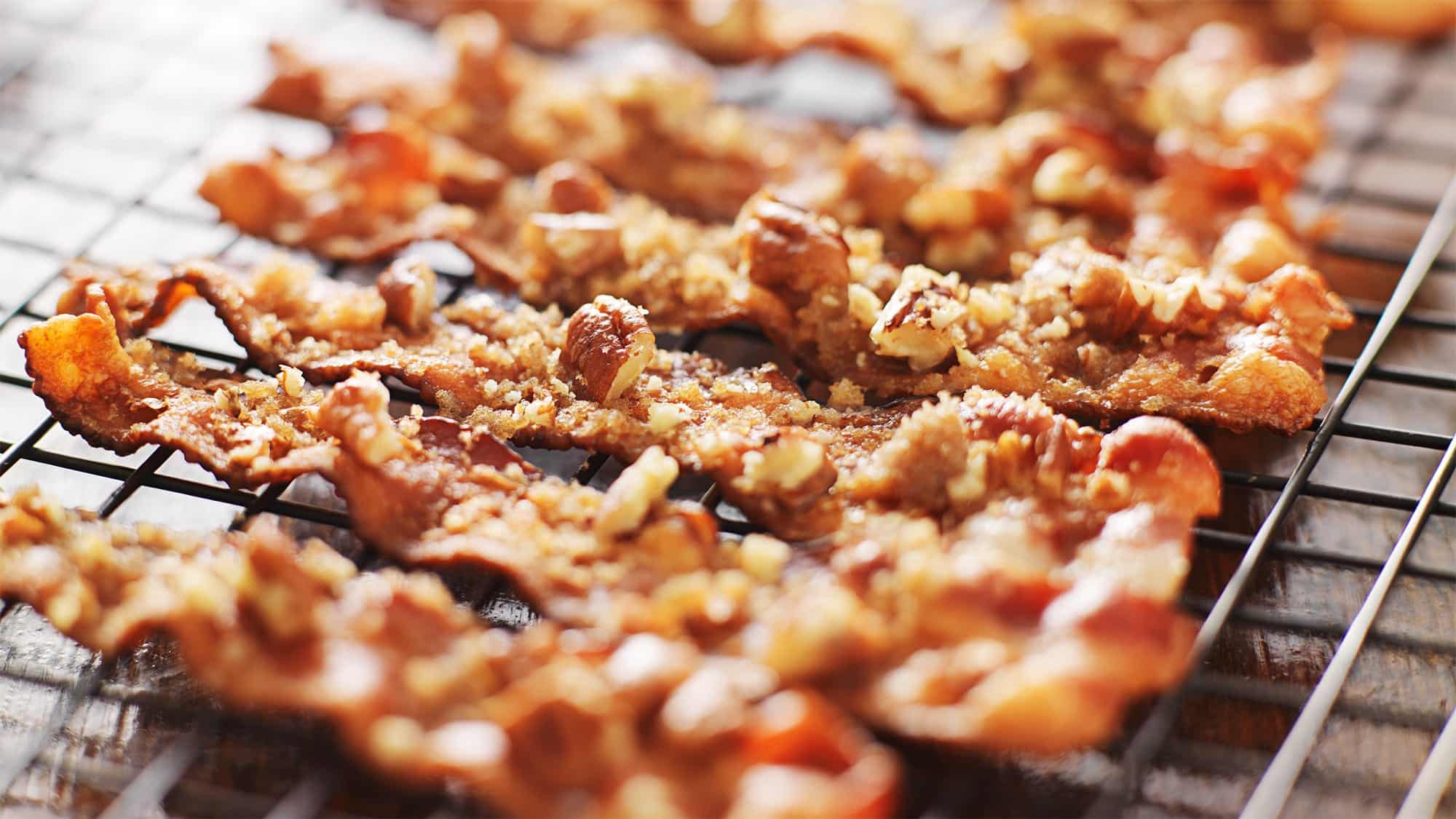 Des tranches de bacon cuites sur une grille au four, caramélisées et piquantes garnies de noix