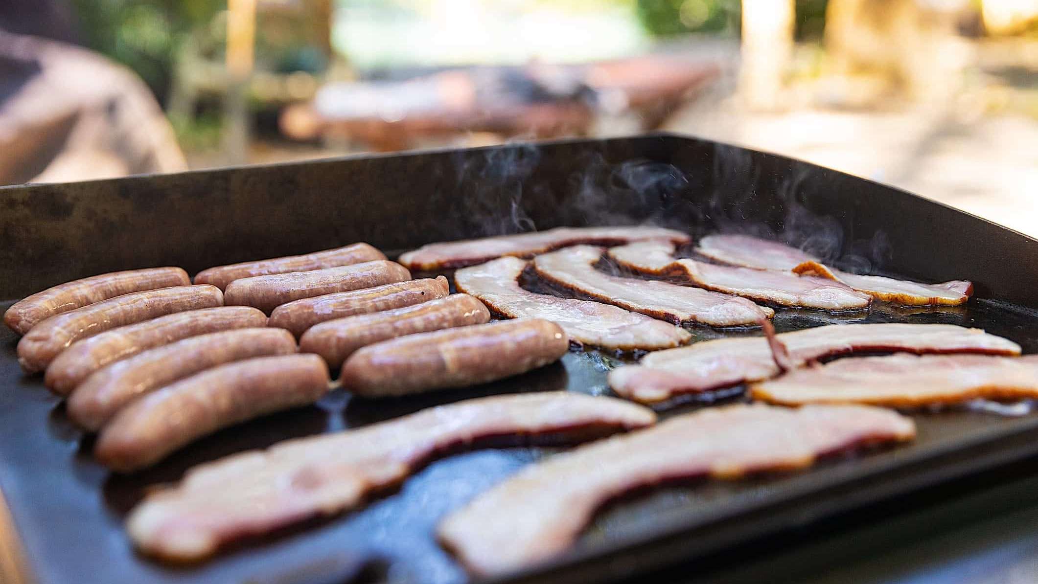Des tranches de bacon et des saucisses cuisent sur une plancha BBQ