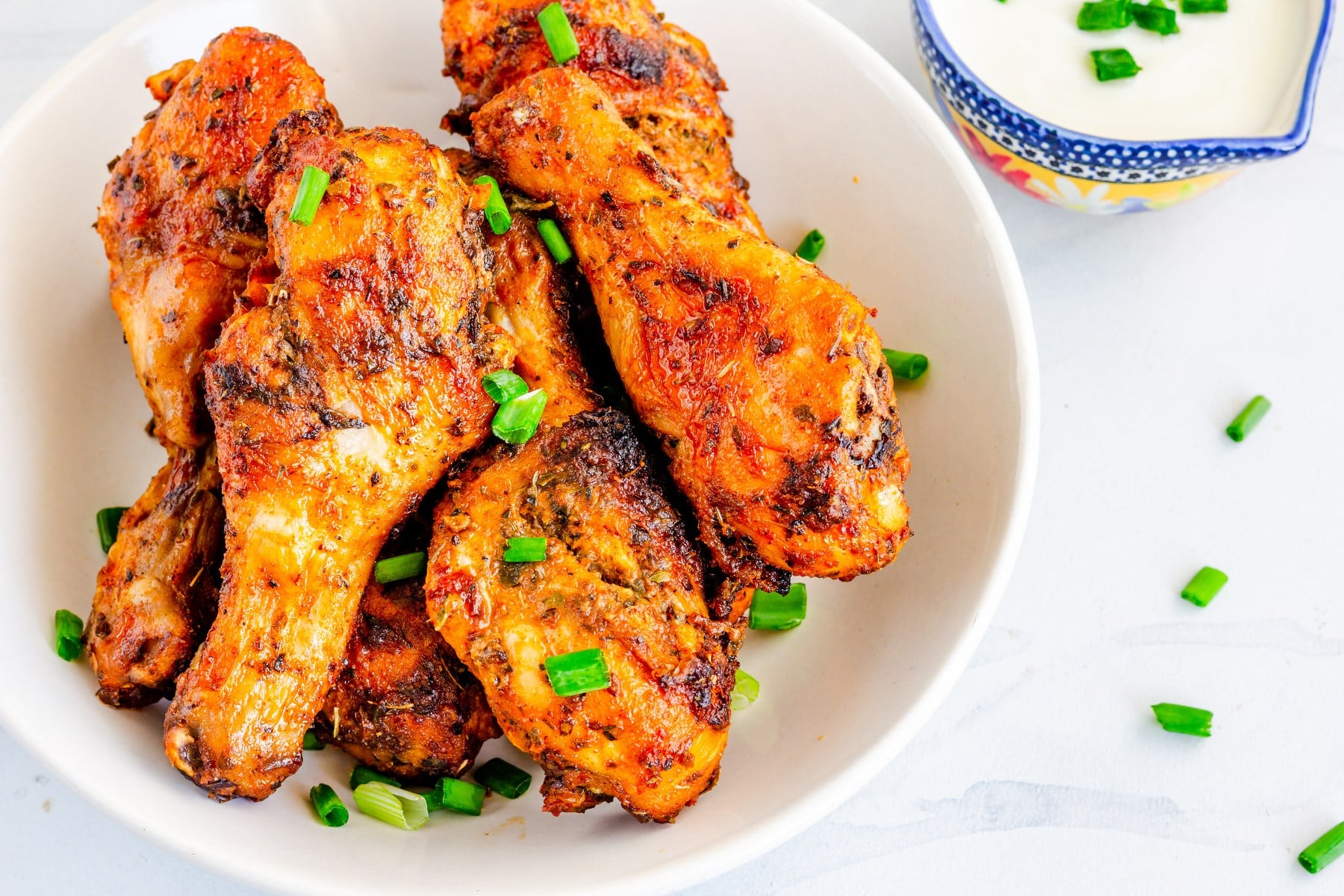 Des pilons de poulet marinés et cuits au BBQ sont posés dans une assiette blanche et garnis de ciboulette ciselée