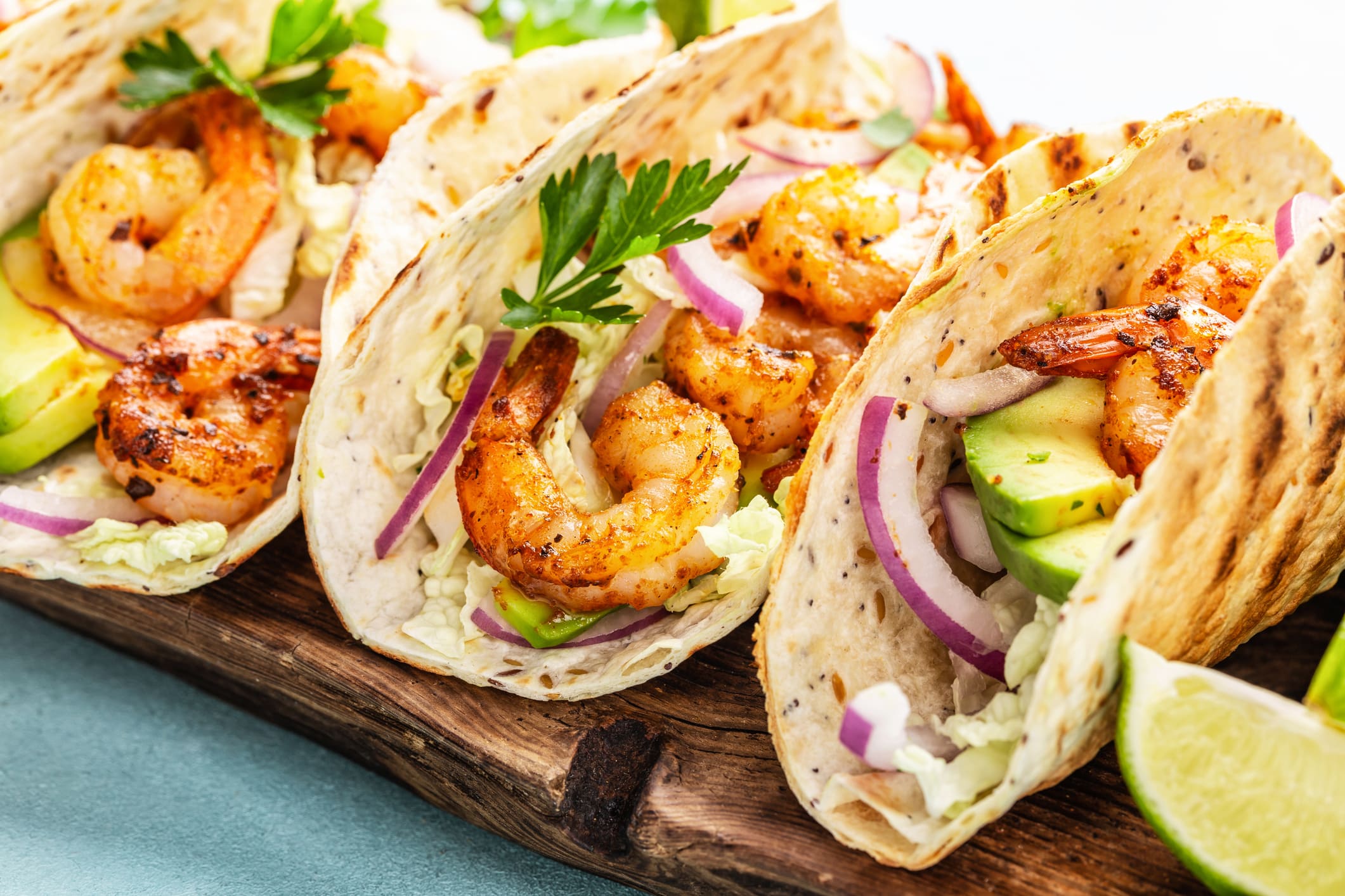 Recettes-mexicaines-BBQ-crevettes 3 tacos de crevettes à la mexicaine grillées au BBQ sont posées sur une planche de bois
