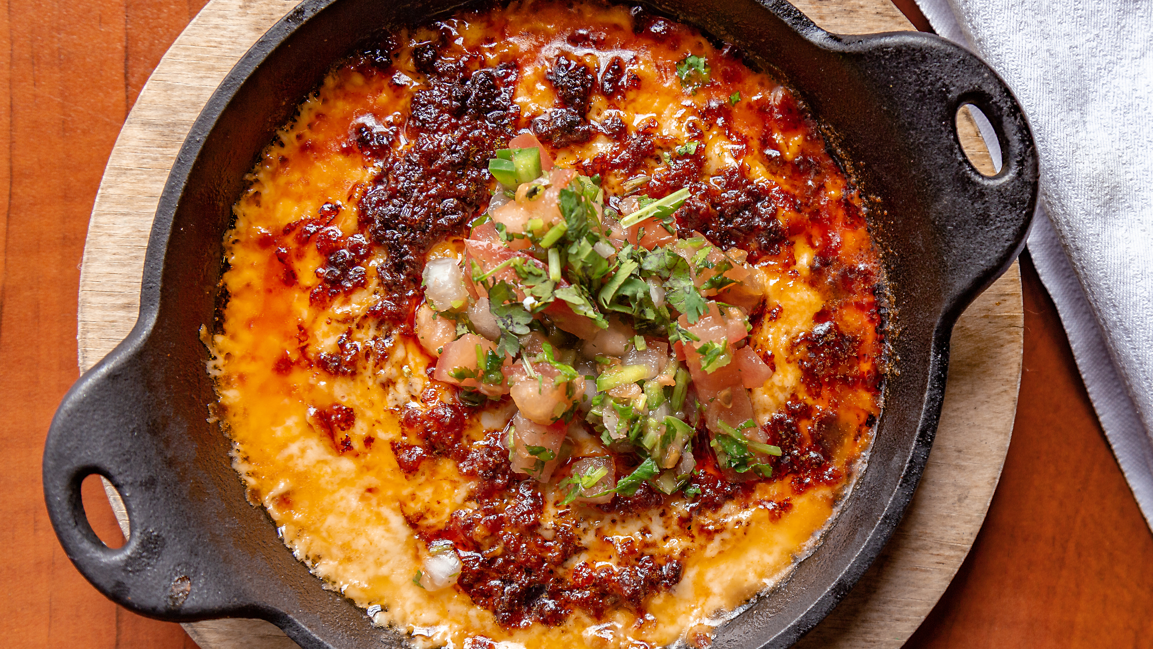 Recettes-mexicaines-BBQ-Queso-Fundido Une cassolette en fonte contient une recette mexicaine au BBQ de queso fundido, du fromage fondu avec de la saucisse chorizo et des légumes
