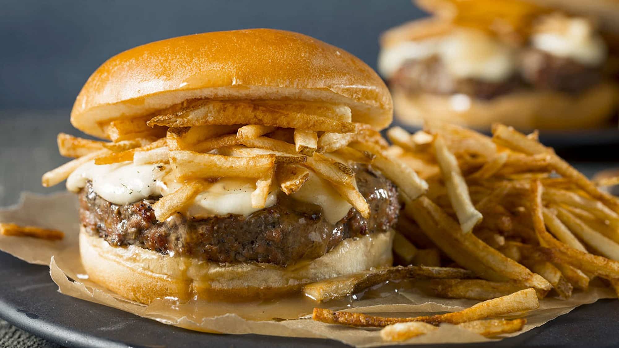 Gros plan sur un burger de boeuf l'épicier au BBQ, garni avec les ingrédients d'une poutine: frites, fromage en grains et sauce brune.