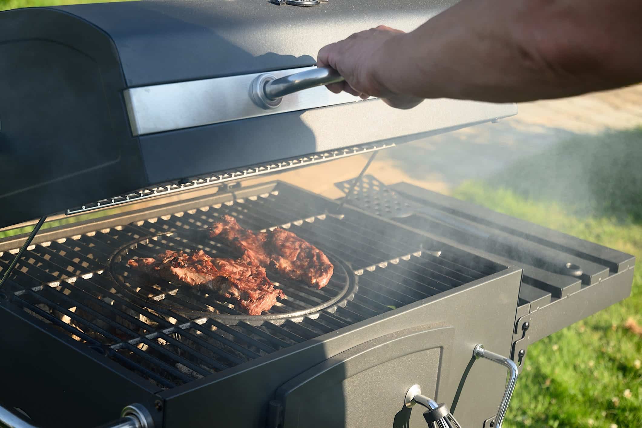 Erreurs-eviter-BBQ-fermer-couvercle Une personne ferme le couvercle d'un BBQ où cuisent des viandes