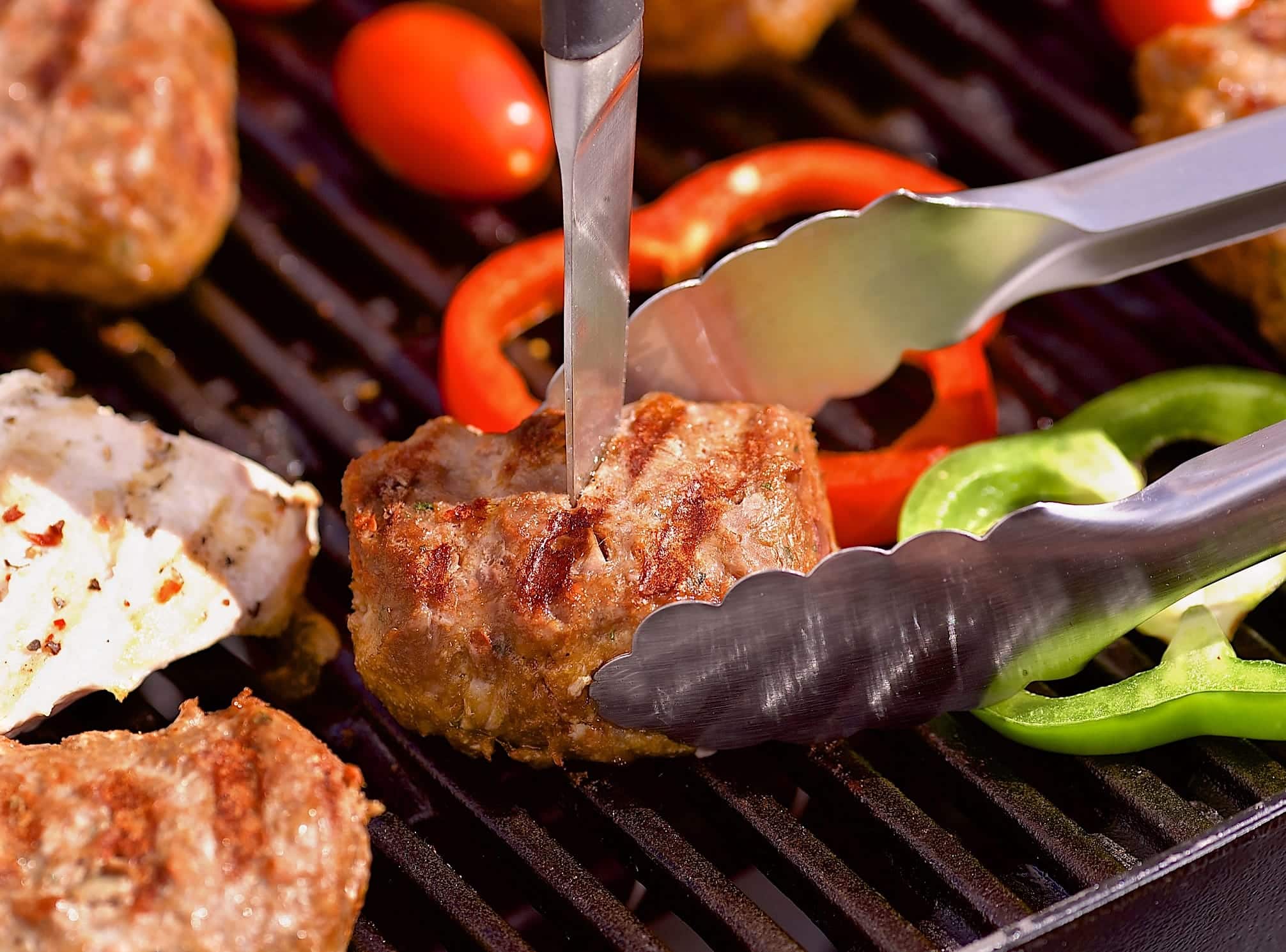 Erreurs-eviter-BBQ-piquer-viande Une personne pique avec un couteau un morceau de viande grillé sur un BBQ