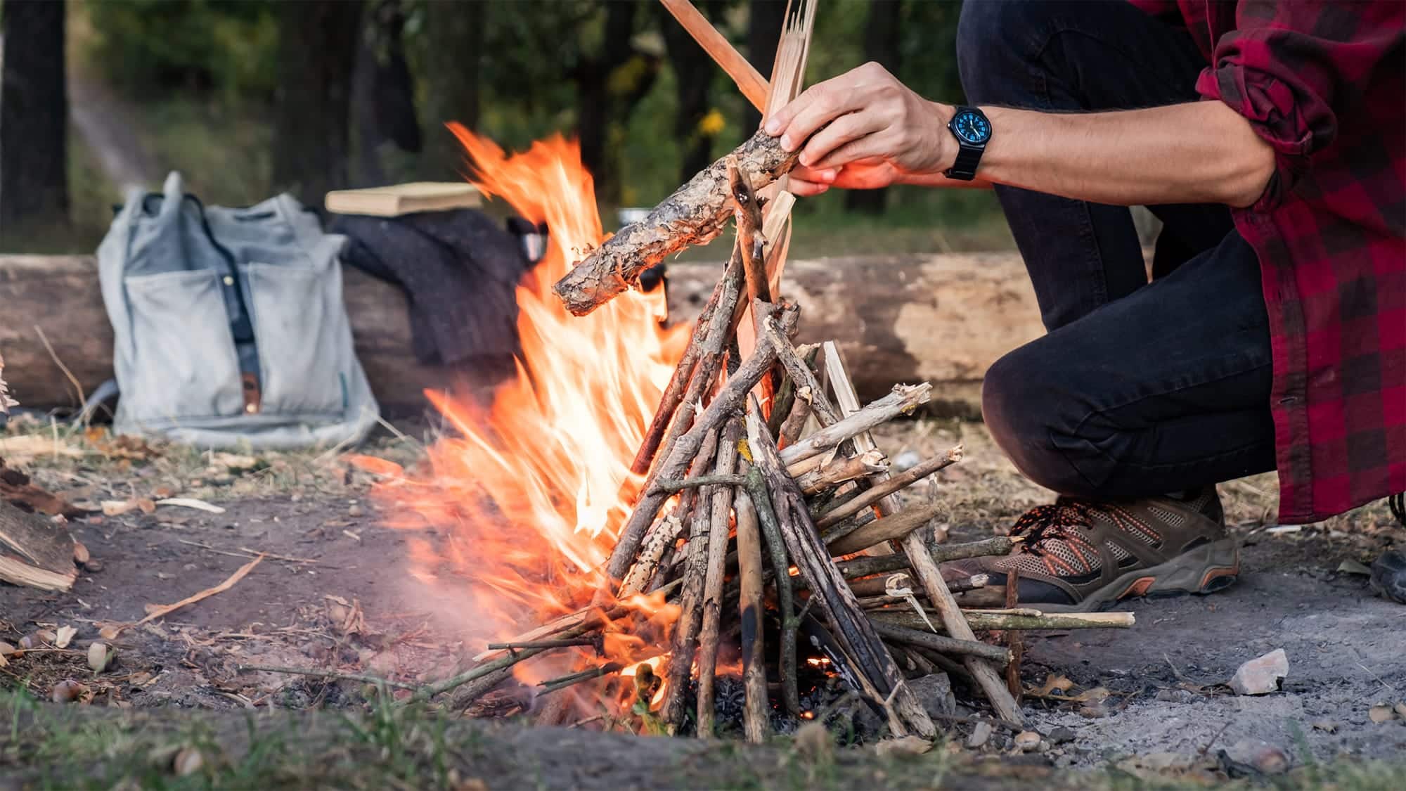 Un homme part un feu de camp avec des petites branches afin de cuisiner en camping