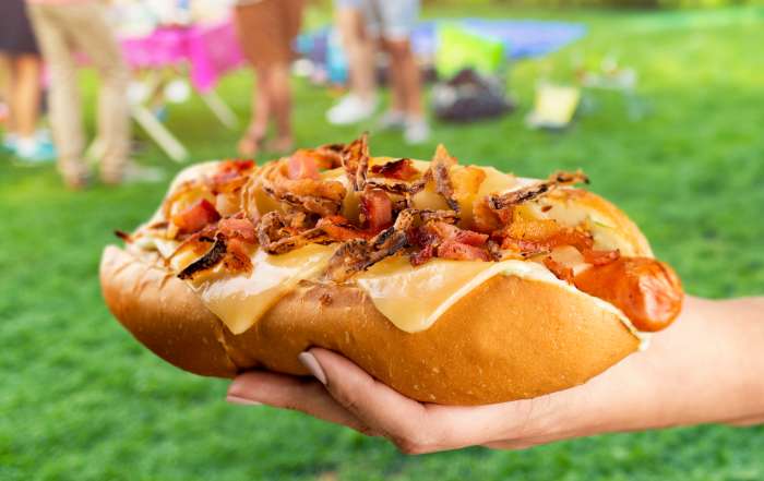 Une main de femme tient un hot-dog gourmet avec les saucisses l'épicier