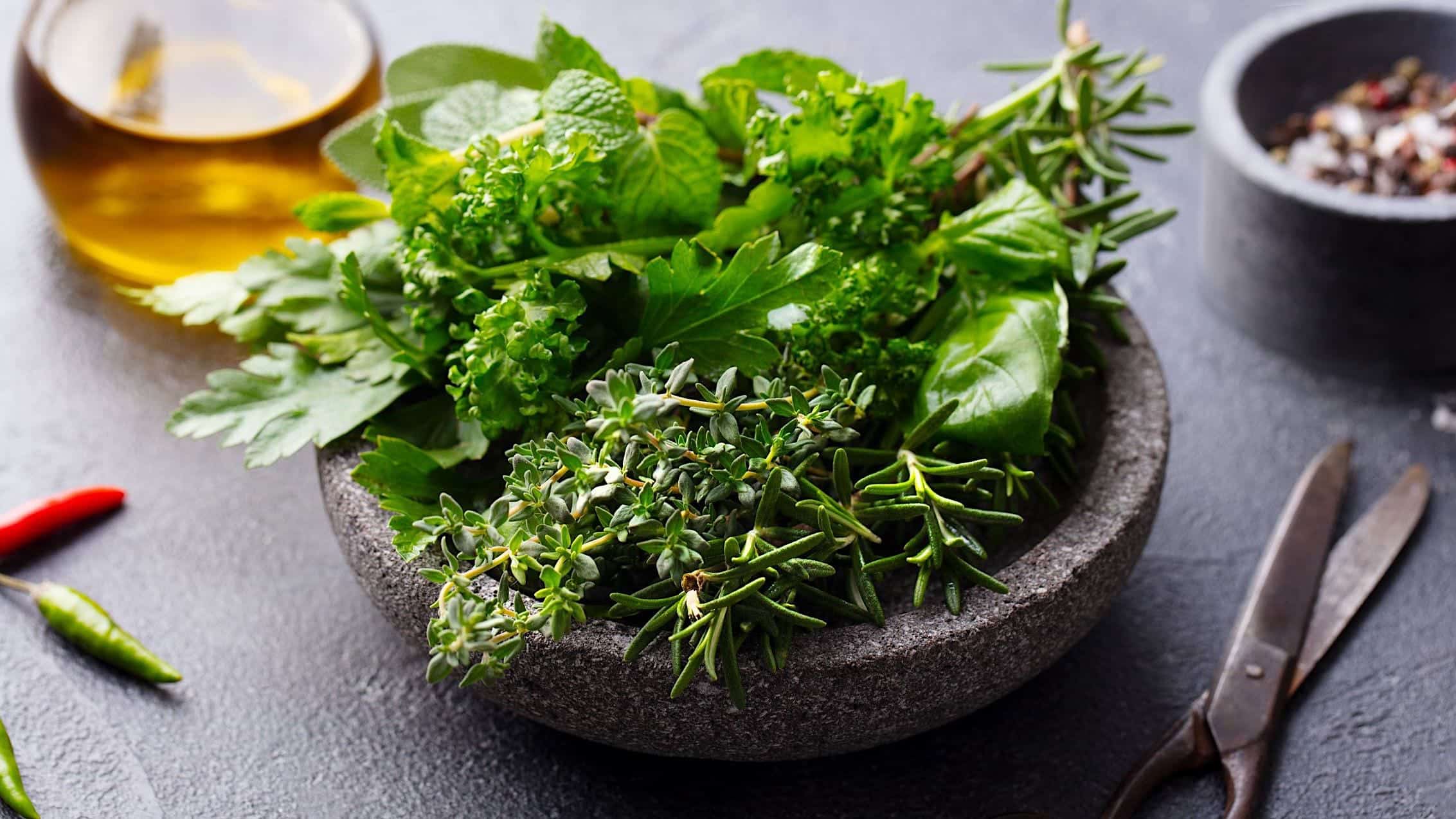 Plusieurs types d'herbes fraîches dans un bol en grès pour assaisonner un poulet rôti sur une canette de bière au BBQ