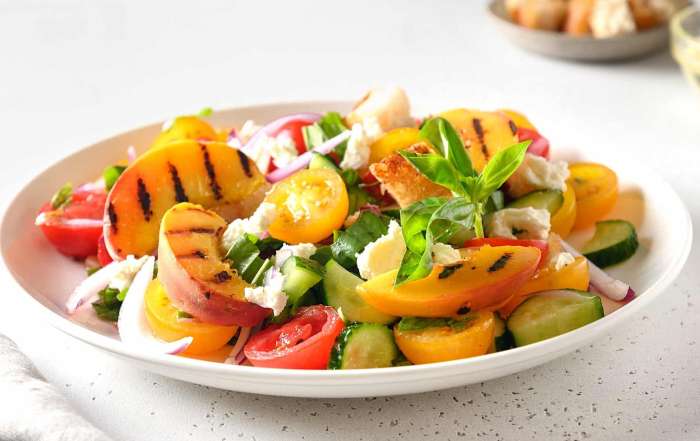 Une salade panzanella avec des pêches et des tomates grillées au BBQ, garnie d'herbes et de fromage