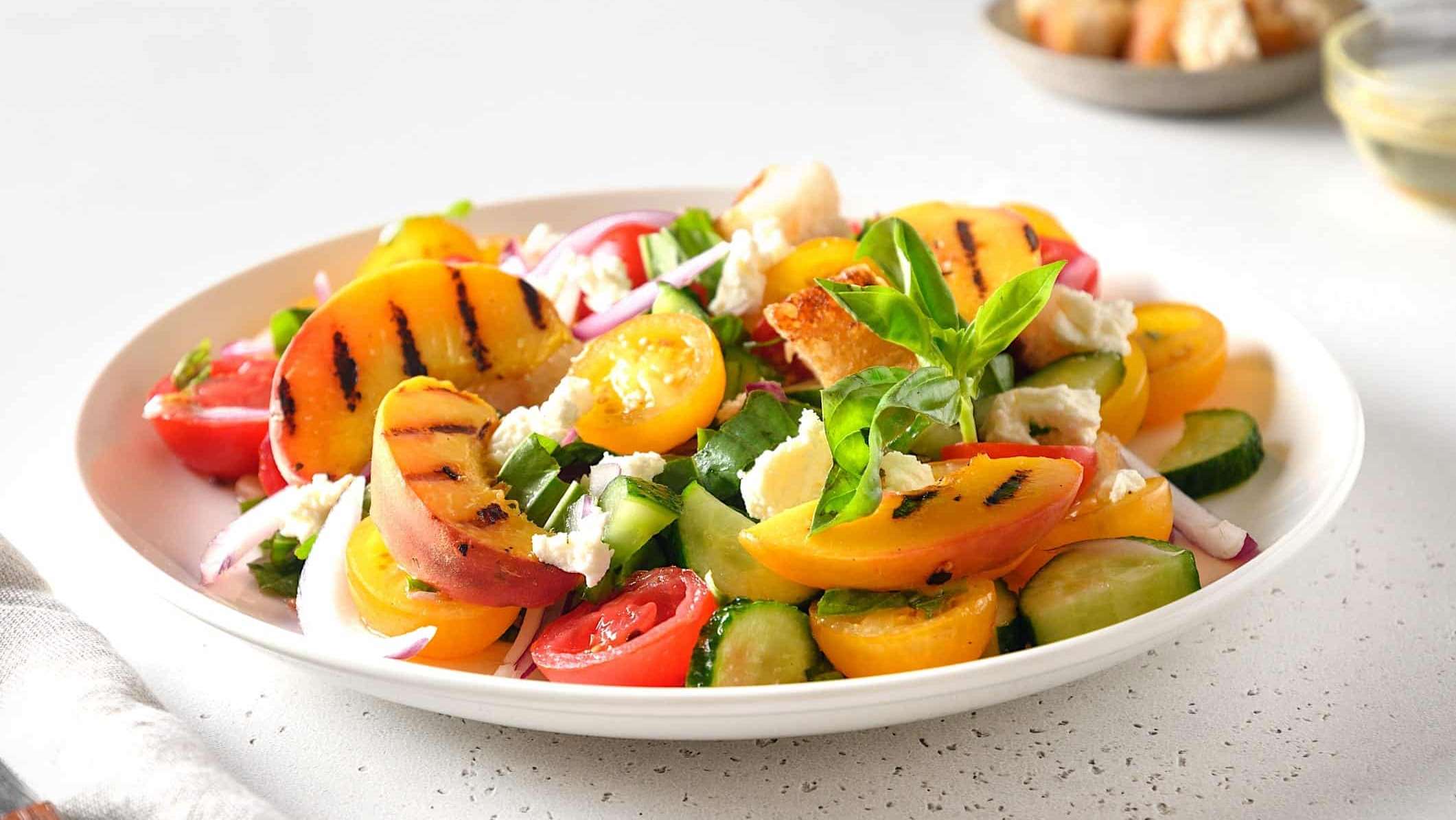 Une salade panzanella avec des pêches et des tomates grillées au BBQ, garnie d'herbes et de fromage