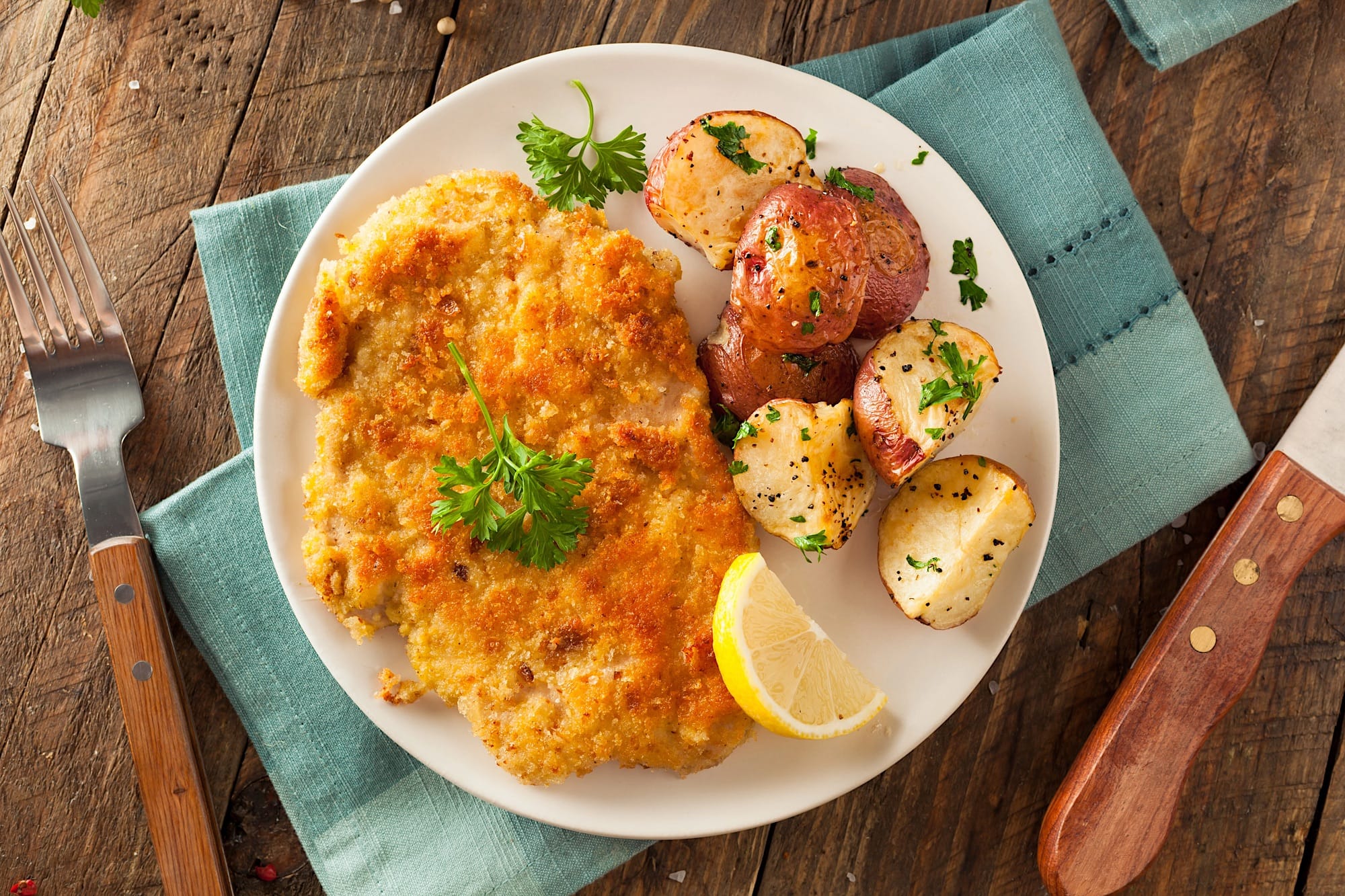 Une assiette blanche posée sur un tissus aqua est garnie d'un bifteck d'intérieur de ronde frit comme du poulet frit, accompagné de pommes de terre grillées et d'une tranche de citron.