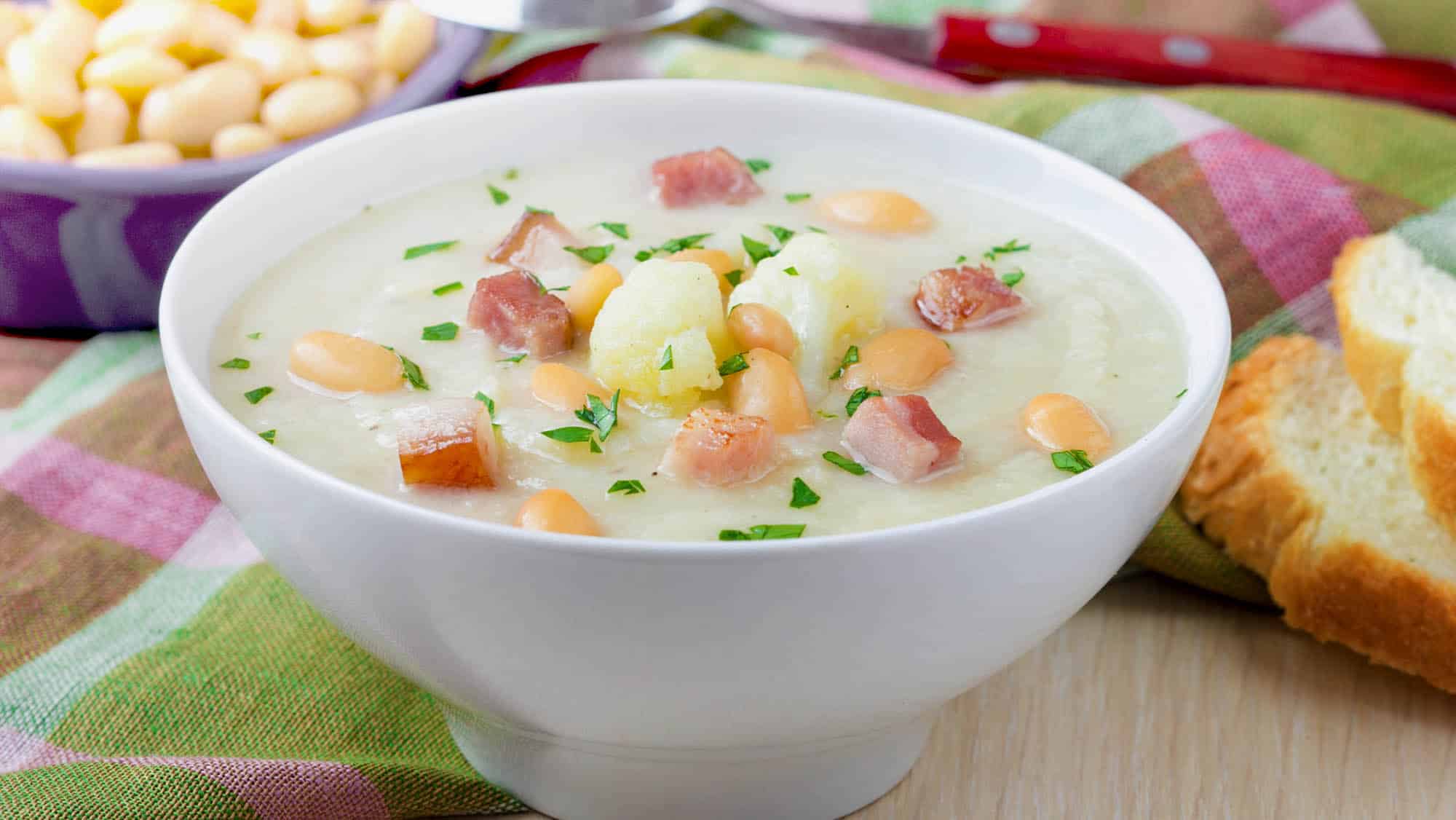 Une recette de soupe-repas réconfortante d'haricots blanc, chou-fleur et jambon, dans un bol blanc