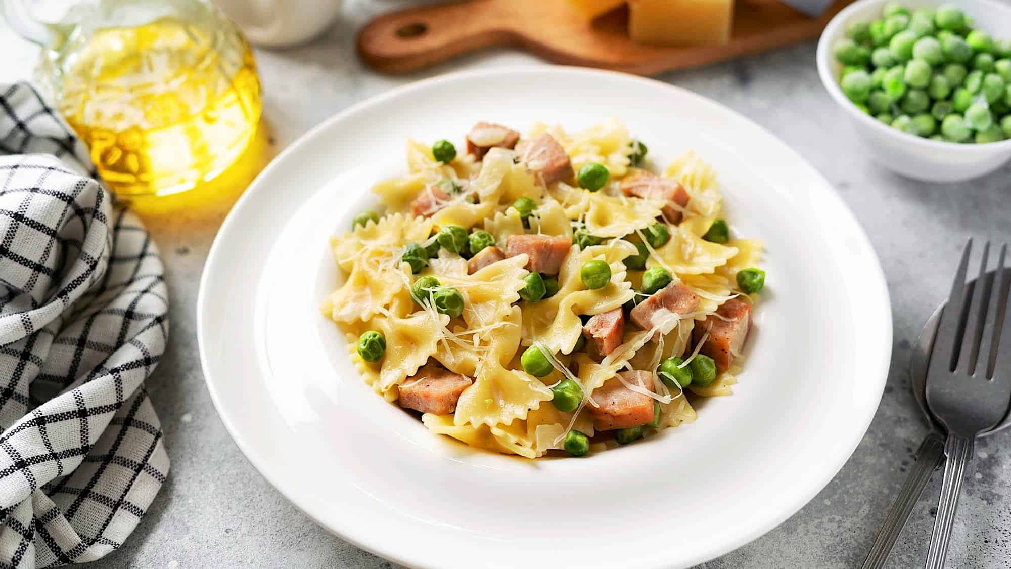 Un bol blanc avec garni d'une recette de pâtes italiennes de farfalle au jambon, petits pois et crème