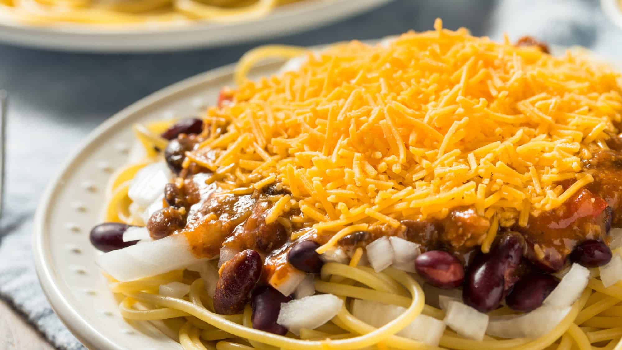 Une assiette de spaghetti et de chili Cincinnati garnirs avec des haricots rouges et des oignons en dés crus.