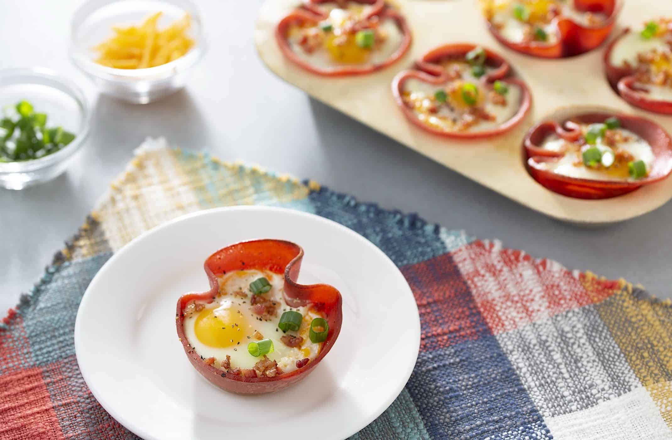 Recettes-déjeuner-enfant-coupes-jambon-oeuf Une assiette blanche avec une coupe de jambon garni d'un oeuf, de bacon et d'oignon vert, une recette de déjeuner amusant à faire avec les enfants.