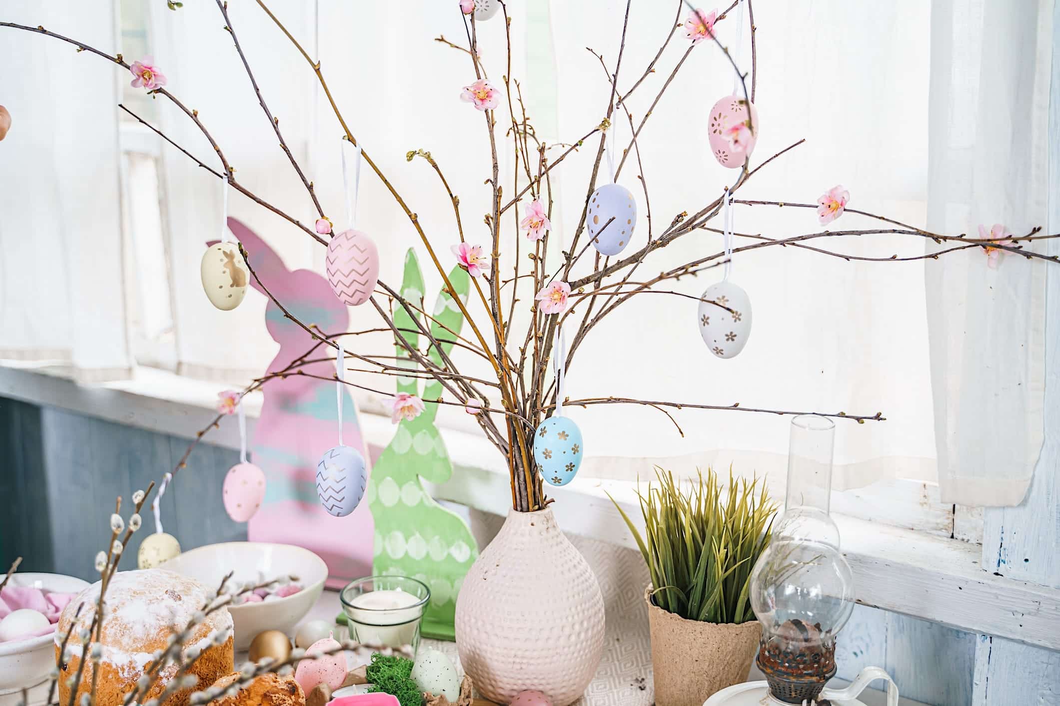 decoration-oeufs-paques-arbre Une décoration de table de Pâques avec des oeufs de Pâques colorés qui ornent des branches d'arbres dans un vase blanc