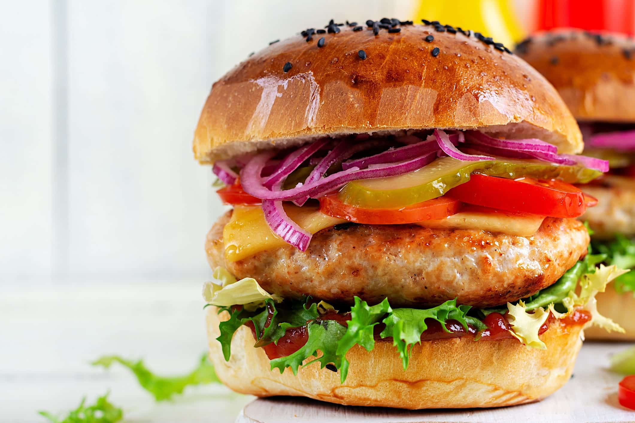 Coupes-porc-BBQ-hache-burger Un burger de porc l'épicier cuit sur le BBQ et garni de laitue, tomate, cornichon, oignon rouge et fromage cheddar dans un pain aux graines de sésame.