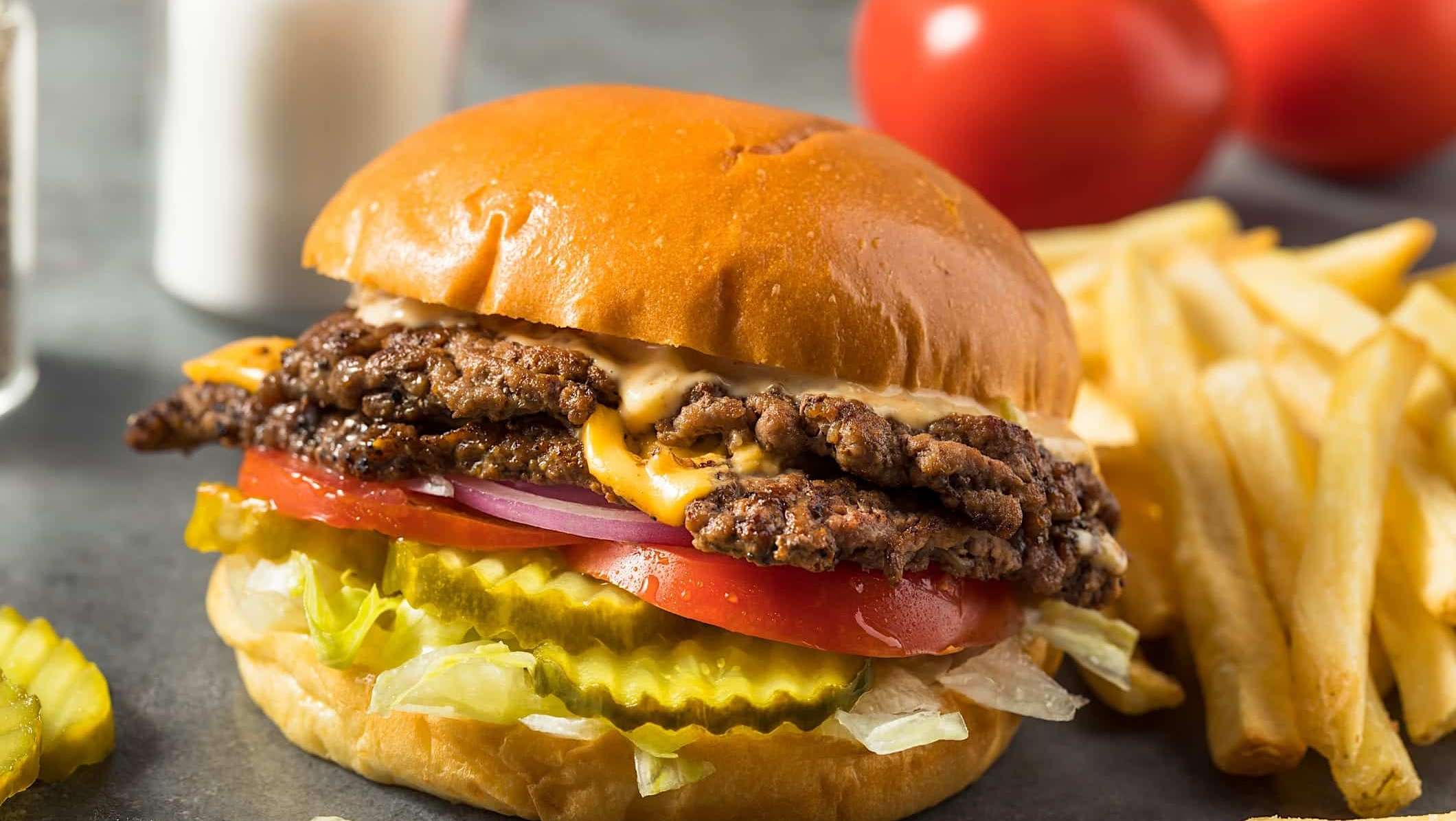 Gros plan d'un smash burger au fromage double accompagné de frites.