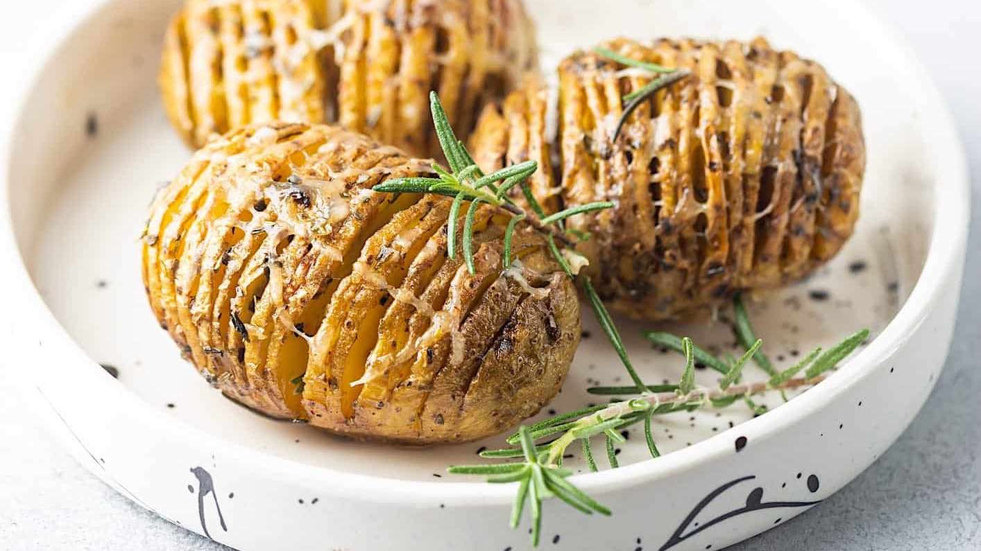 recettes-pommes-de-terre-BBQ-Hasselback Des pommes de terres coupées à la hasselback et grillées sur le BBQ sont posées dans une assiette blanche et garnies de romarin frais.