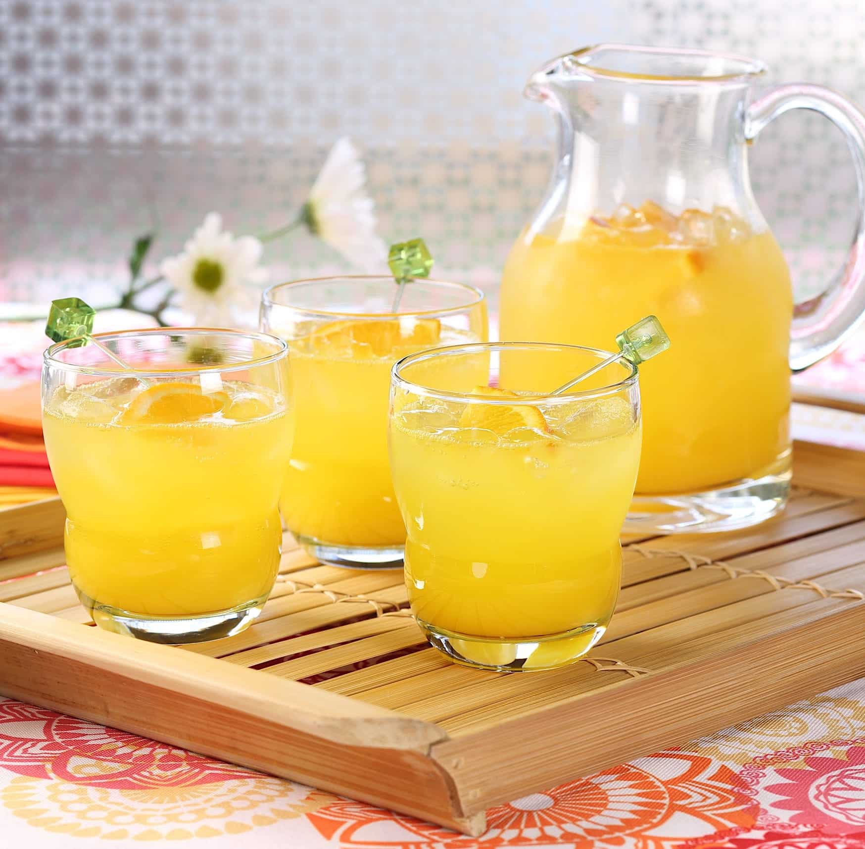 Sangria-recette-mangue Un pichet et 3 verres de sangria à la mangue et orange sont posés sur un cabaret en bambou pour une recette de sangria originale