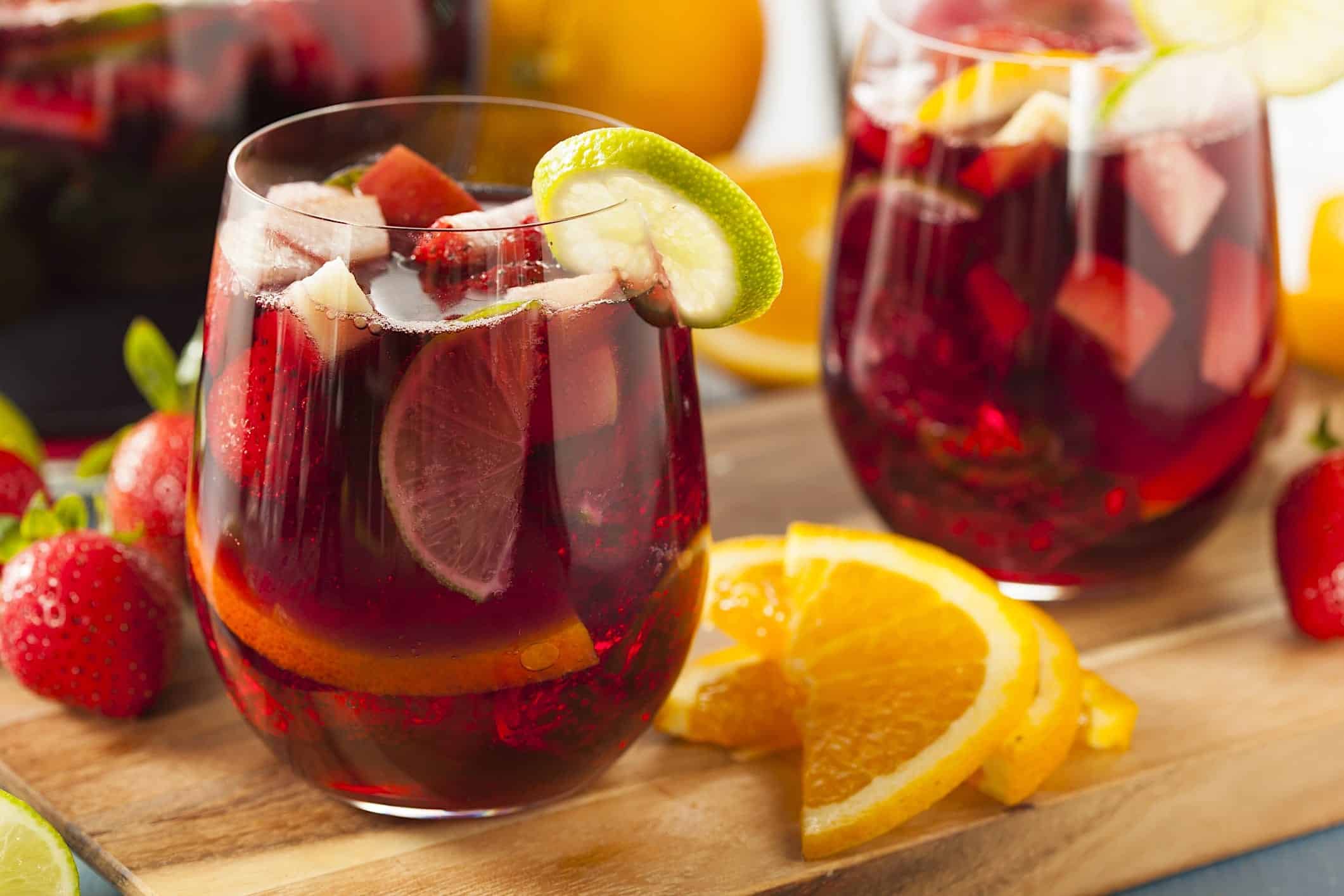 recette-sangria-traditionnelle-verres 2 verres de sangria classique garnis de tranches de lime, de citron et des fraises entières qui font partie de la recette