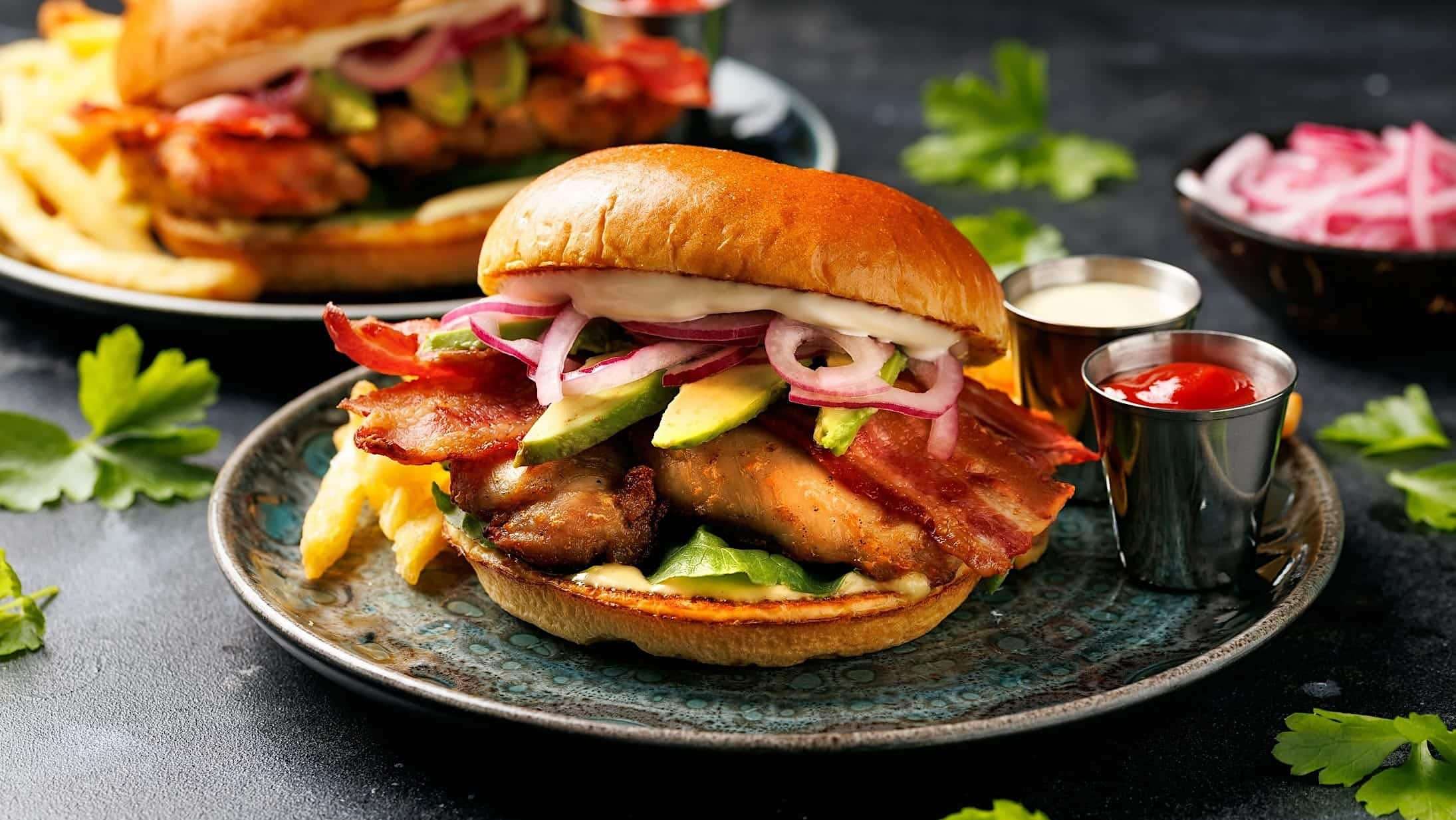 recettes-poitrine-poulet_burger Un burger de poitrine de poulet grillée garni de laitue, d'avocat, de bacon, d'oignon rouge et de tomate