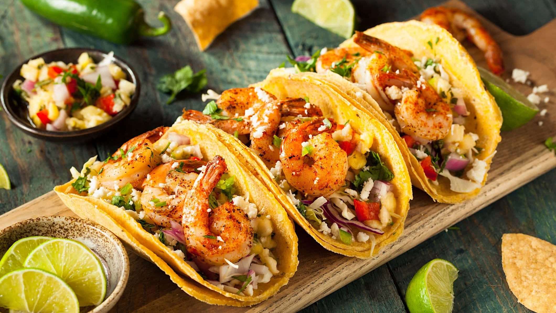 3 tacos de crevettes marinées et grillées au BBQ sont dressés sur une planche de bois et accompagnées de pico de gallo à l'ananas.
