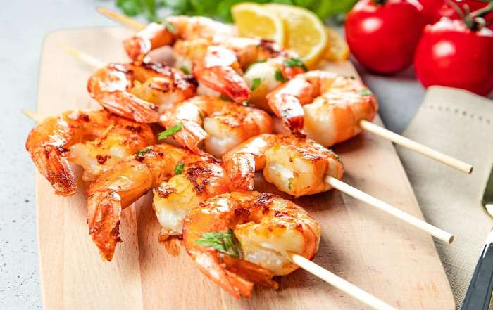 3 brochettes de crevettes marinées et grillées au BBQ sont dressées sur une planche de bois.