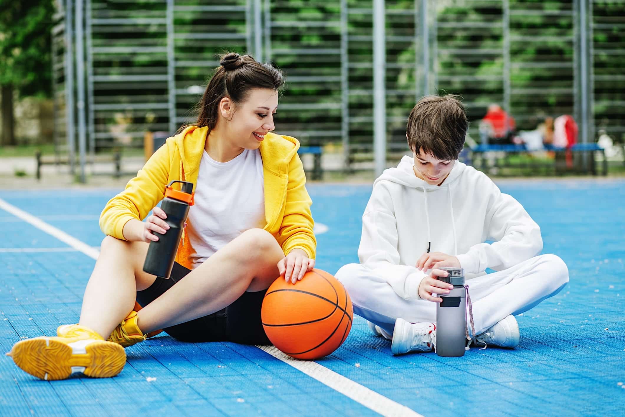 lunch-adolescent-nutritif-gars-fille Deux adolescents sont assis sur un court de basketball et tiennent leur gourde d'eau pour illustrer l'importance de s'hydrater