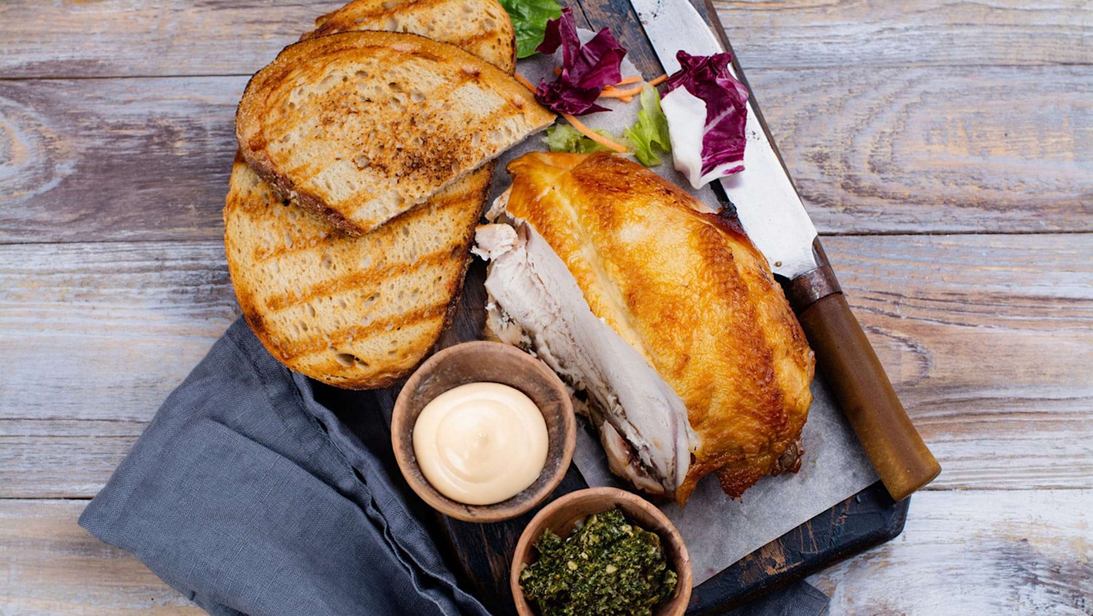 sandwich-restes-viandes-poulet roti Un demi poulet rôti est posé sur une planche de marbre avec des ingrédients pour créer des sandwichs gourmets avec des restes de viande.
