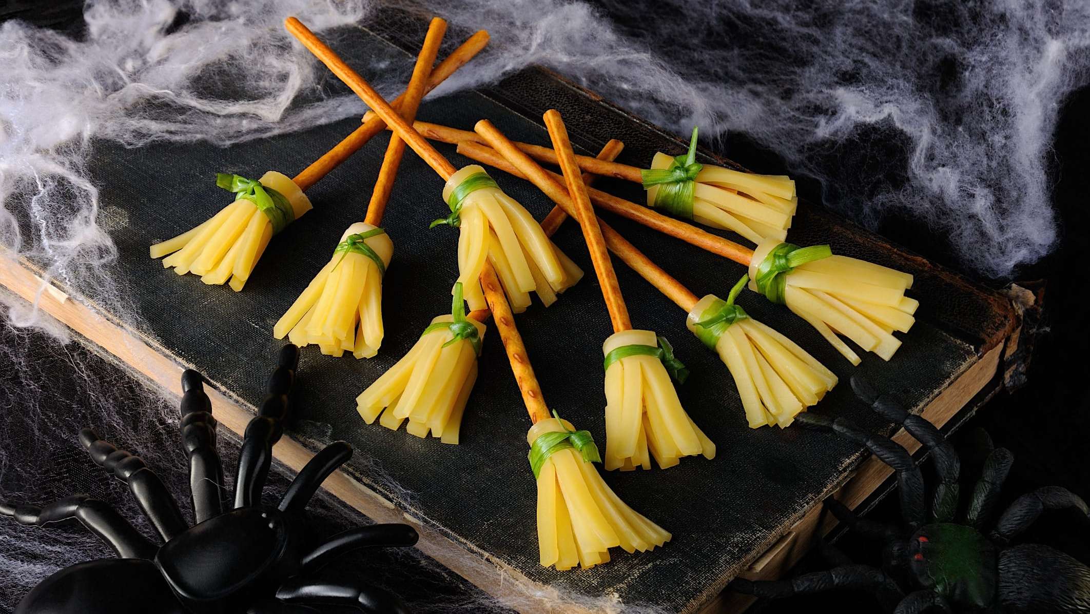 boite-lunch-halloween-balais-sorciere Une assiette de pierre noire est posée dans un décor d'Halloween et des balais de sorcière faits de bâtonnets de pretzel et de fromage à effilocher y sont dressés pour une idée de boite à lunch d'Halloween